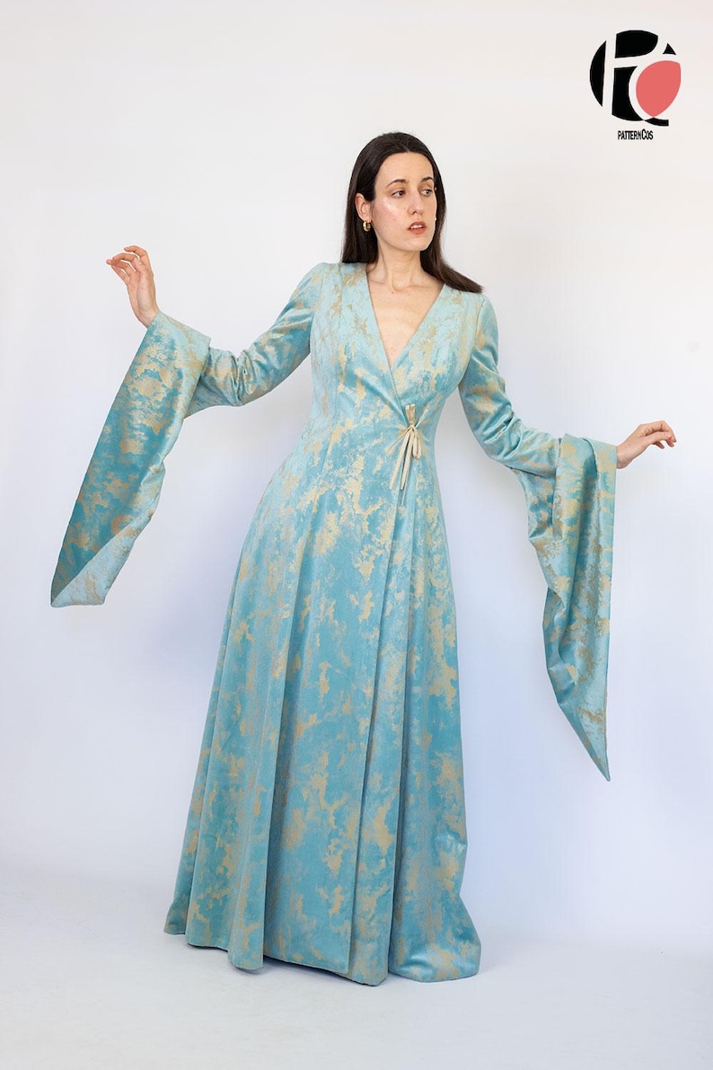 May include: A long, flowing dress in a light blue hue with a gold pattern. The dress features long, flared sleeves and a V-neckline. A gold-colored tie cinches the waist. The dress is made of a soft, velvety fabric, perfect for a special occasion.