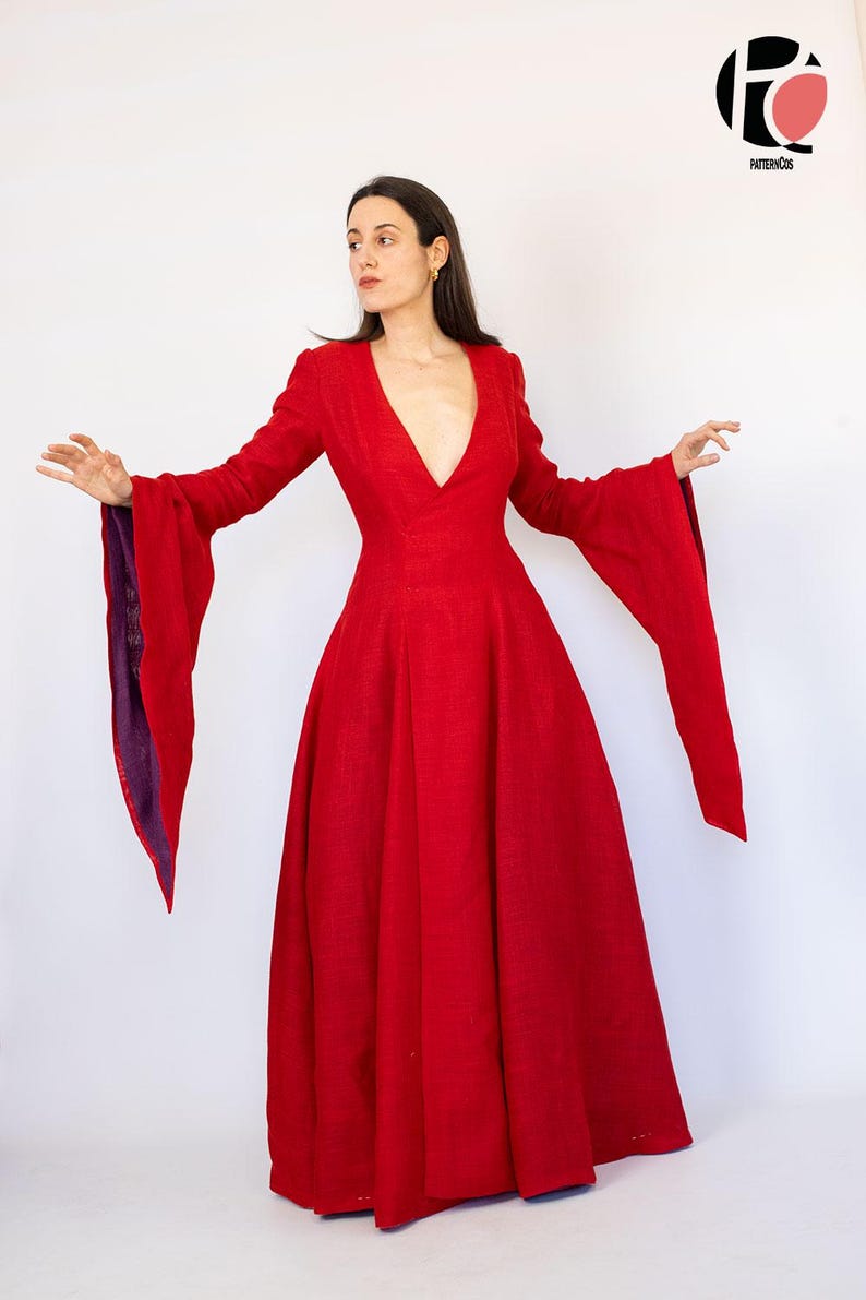 May include: A long, flowing red dress with a deep V-neck and dramatic bell sleeves. The sleeves have a purple lining. The dress is floor-length and made of a textured fabric. The dress is a bold statement piece.