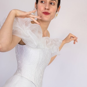 May include: A white off-the-shoulder corset with a ruffled overlay and a white skirt. The corset has a floral pattern.