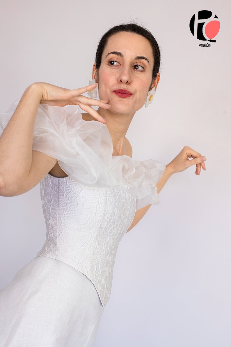 May include: A white off-the-shoulder corset with a ruffled overlay and a white skirt. The corset has a floral pattern.