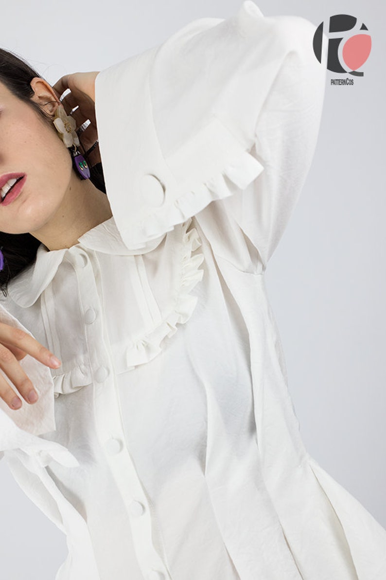May include: A white button-up shirt with a ruffled collar and cuffs. The shirt has a relaxed fit and is made of a lightweight fabric.
