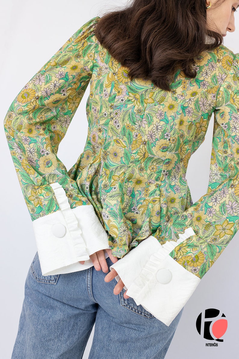 May include: A yellow and green floral print blouse with long sleeves and white ruffled cuffs. The cuffs have a button closure.