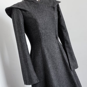 May include: A long-sleeved gray dress with a high collar and a fitted bodice. The dress has a flared skirt and a unique shoulder design.