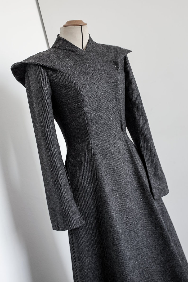 May include: A long-sleeved gray dress with a high collar and a fitted bodice. The dress has a flared skirt and a unique shoulder design.