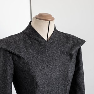May include: A gray wool dress with a high collar and a V-neckline. The dress has a fitted bodice and a full skirt.