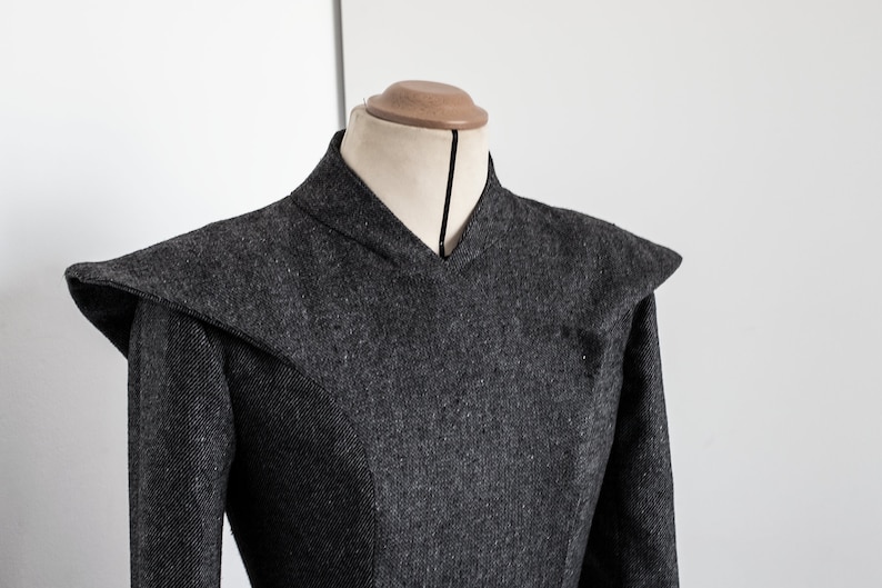 May include: A gray wool dress with a high collar and a V-neckline. The dress has a fitted bodice and a full skirt.