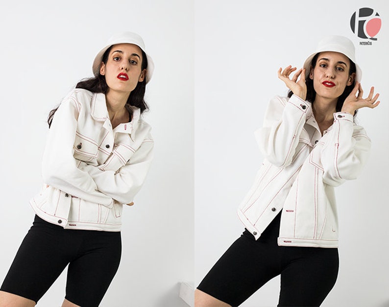 Pu&ograve; includere: Una donna indossa una giacca di jeans bianca con cuciture rosse, pantaloncini da ciclista neri e un cappello a secchiello bianco. Sta posando con le mani sulla testa.