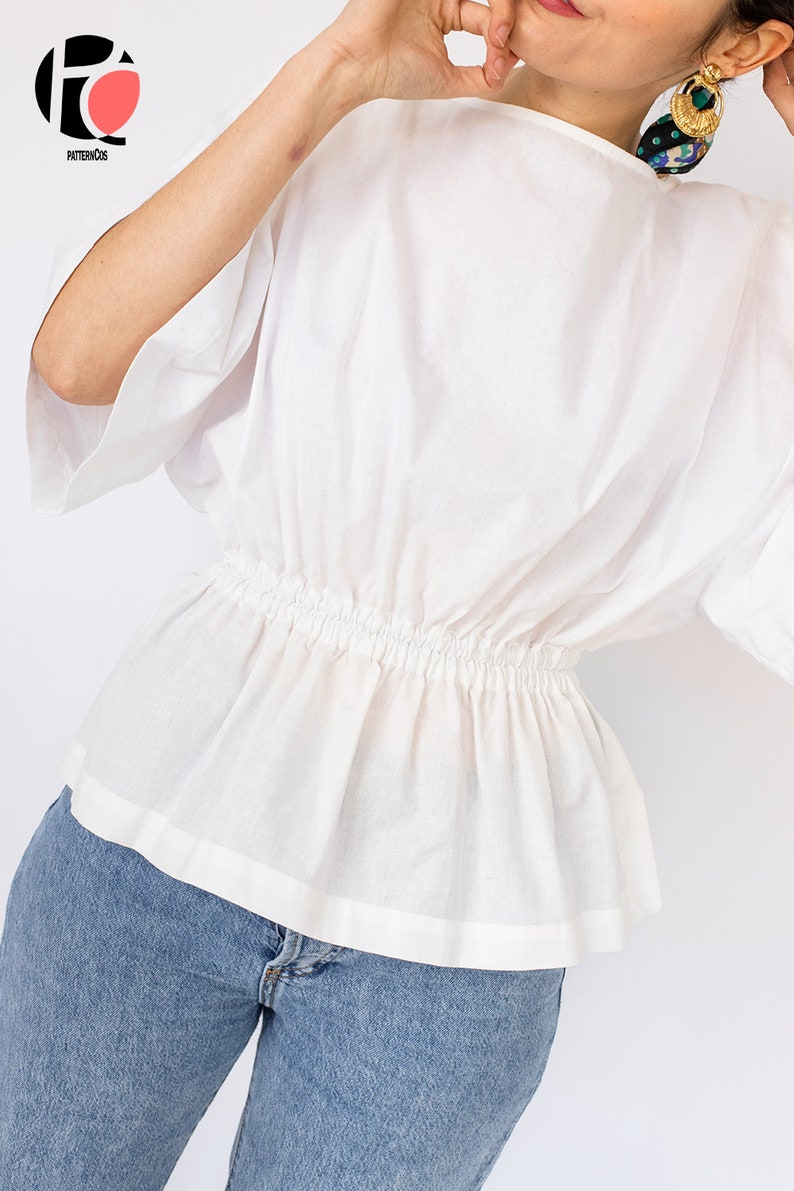 May include: A white, short-sleeved blouse with a gathered elastic waistband. The blouse is made of a lightweight fabric and has a relaxed fit.