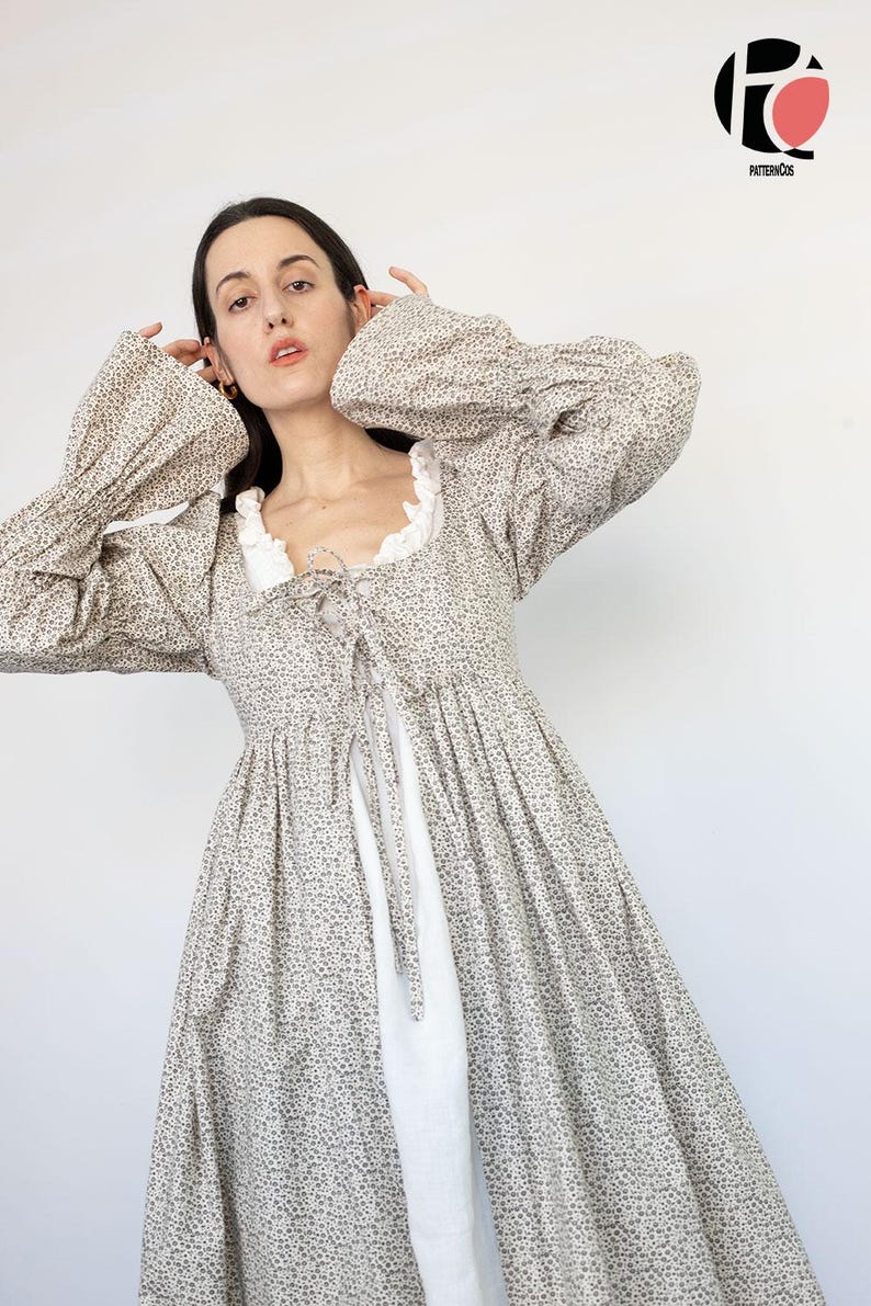 May include: A long-sleeved dress with a floral pattern in shades of gray and white. The dress features a square neckline with a white lace trim and a tie-up front. The sleeves are long and voluminous. The dress is a vintage style.