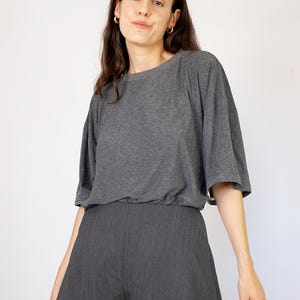 May include: A woman wearing a gray short-sleeved t-shirt and gray shorts. The t-shirt has a relaxed fit and the shorts have a wide leg.