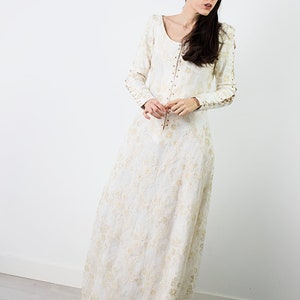 Peut inclure: Une robe maxi blanche &agrave; motif floral et manches longues. La robe a un col rond et une fermeture boutonn&eacute;e sur le devant.