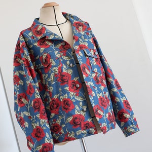 Pu&ograve; includere: Una giacca di jeans blu con stampa di rose rosse. La giacca ha una chiusura con bottoni e maniche lunghe.