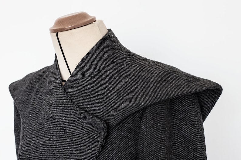 May include: A gray hooded jacket with a unique collar design. The jacket is made of a textured fabric and has a relaxed fit.