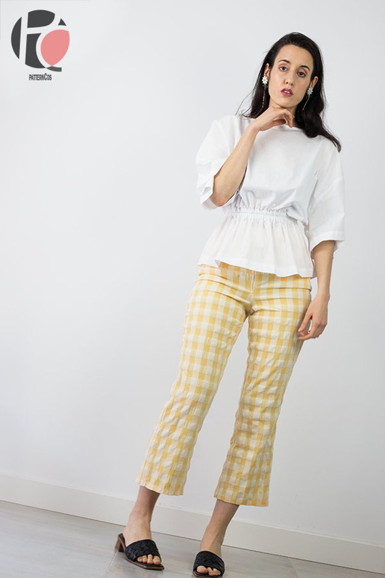 May include: A woman wearing a white, loose-fitting blouse with a gathered waist and yellow and white gingham pants. She is wearing black heeled sandals.