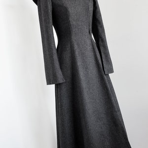 May include: A gray wool dress with a fitted bodice and a flared skirt. The dress has a high neckline and long sleeves with a unique, pointed shoulder detail.