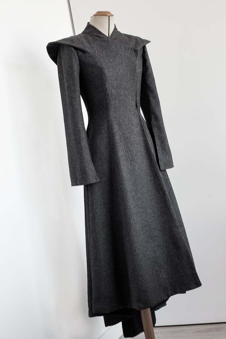 May include: A gray wool dress with a fitted bodice and a flared skirt. The dress has a high neckline and long sleeves with a unique, pointed shoulder detail.
