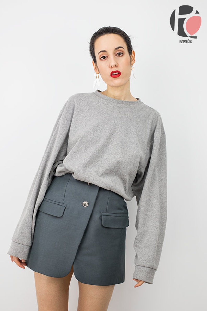 May include: A woman wearing a gray long-sleeved sweatshirt and a dark gray skirt with a button closure. The skirt has two pockets on the front.