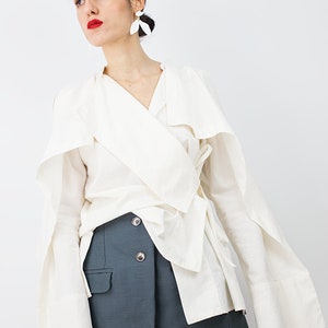 May include: A white wrap blouse with long sleeves and a tie at the waist, paired with a dark blue skirt. The blouse has a wide collar and the skirt has a button closure.
