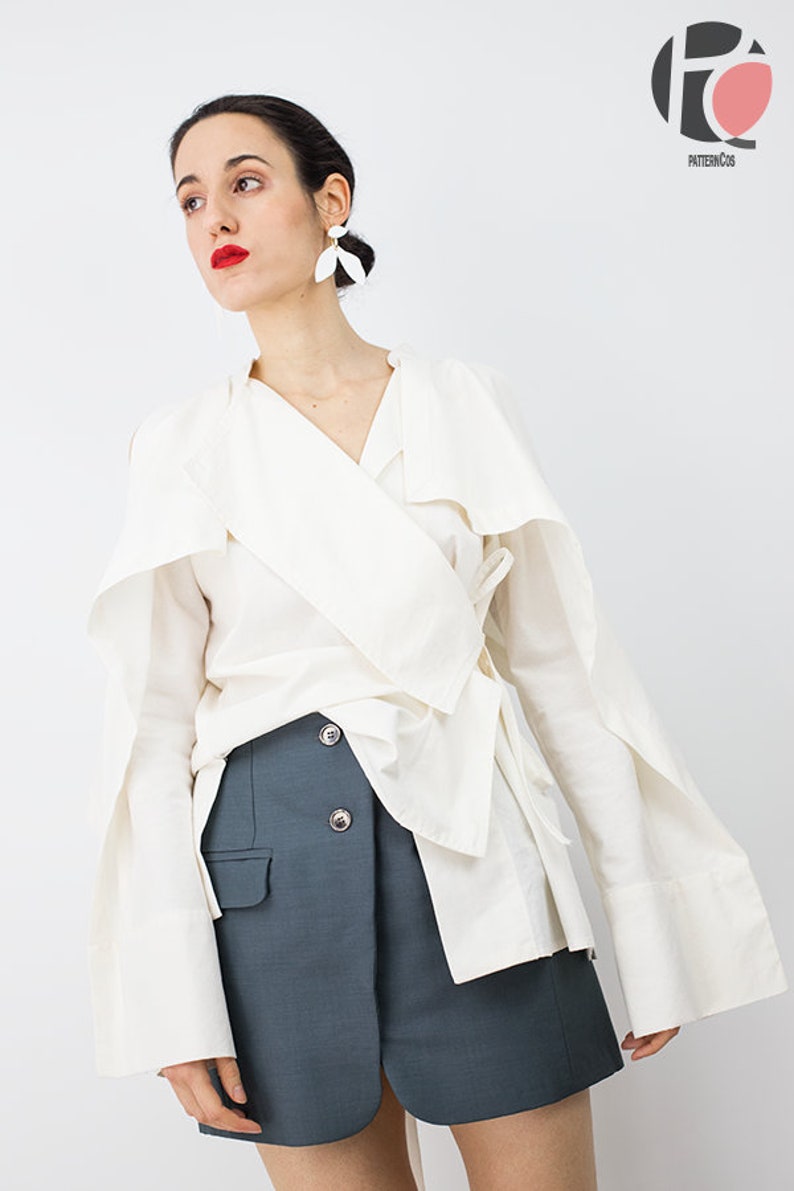 May include: A white wrap blouse with long sleeves and a tie at the waist, paired with a dark blue skirt. The blouse has a wide collar and the skirt has a button closure.