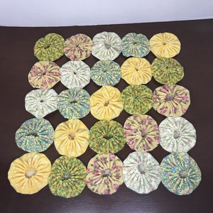 May include: A yellow, green, and pink floral fabric quilt square with 25 individual circles sewn together. Each circle has a ruffled edge and a different floral pattern.