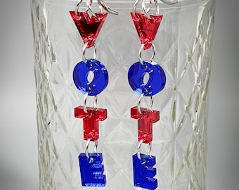 May include: A pair of dangle earrings featuring the word "VOTE" in red and blue acrylic letters. The earrings are suspended from silver hooks.