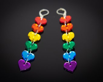 Könnte beinhalten: Ein Paar Regenbogen-Herz-Ohrringe. Jeder Ohrring hat eine Kette aus sieben Herzen in den Farben des Regenbogens, von Rot bis Lila.