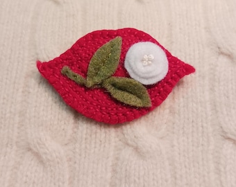 May include: A red felt leaf with a white felt flower and green felt leaves. The flower has a small pearl-like center.