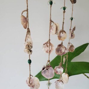 Peut inclure: Un carillon &eacute;olien artisanal compos&eacute; de coquillages suspendus &agrave; un morceau de bois flott&eacute;. Le carillon est orn&eacute; de divers coquillages, de perles vertes et d'&eacute;l&eacute;ments en verre transparent, le tout sur de la ficelle naturelle.
