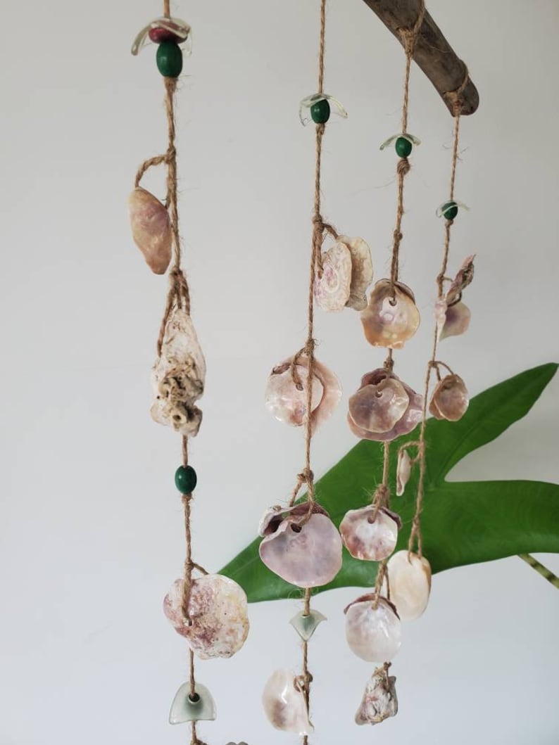 Peut inclure: Un carillon &eacute;olien artisanal compos&eacute; de coquillages suspendus &agrave; un morceau de bois flott&eacute;. Le carillon est orn&eacute; de divers coquillages, de perles vertes et d'&eacute;l&eacute;ments en verre transparent, le tout sur de la ficelle naturelle.
