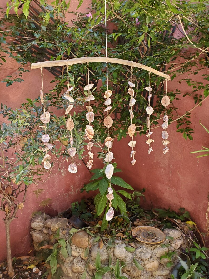 Peut inclure: Mobile artisanal de coquillages suspendu &agrave; une branche de bois incurv&eacute;e. Le mobile est compos&eacute; de coquillages de diff&eacute;rentes tailles et formes, reli&eacute;s par de la ficelle naturelle. Les coquillages sont principalement blancs et beiges, pour un style c&ocirc;tier.