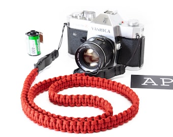 May include: A red paracord camera strap with a silver YASHICA camera and a roll of film.