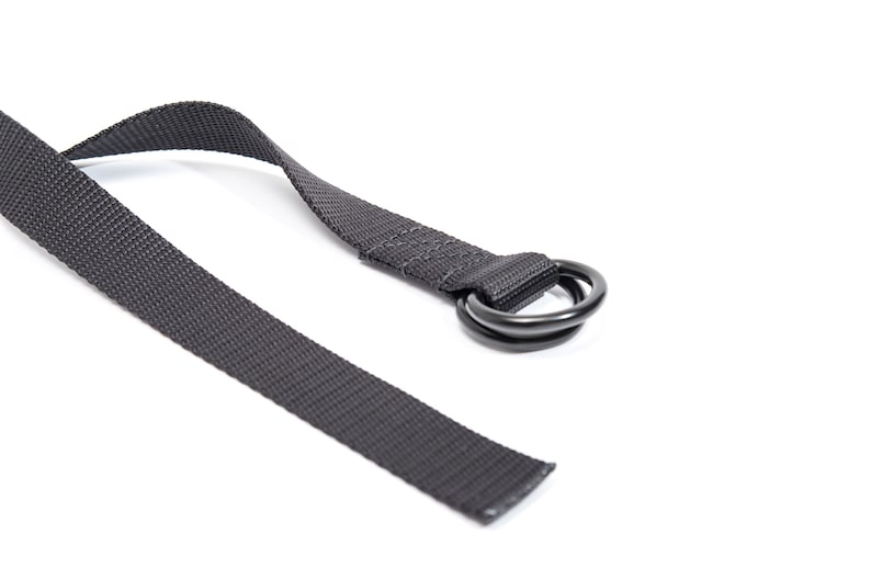 K&ouml;nnte beinhalten: Ein schwarzes Nylonband mit einem schwarzen Doppelring aus Metall.