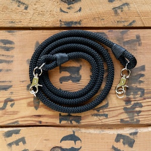 May include: Black camera strap made of braided rope with two silver metal clasps.
