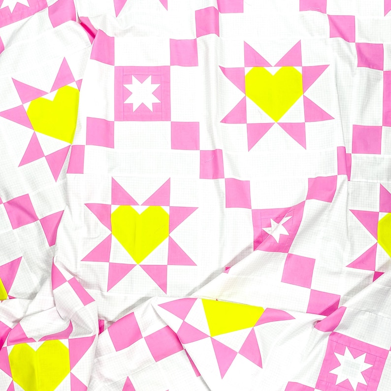 Puede incluir: Colcha blanca con un patr&oacute;n repetitivo de estrellas rosas, corazones amarillos y estrellas blancas. La colcha est&aacute; hecha de un material suave, posiblemente algod&oacute;n. El dise&ntilde;o es moderno y geom&eacute;trico.