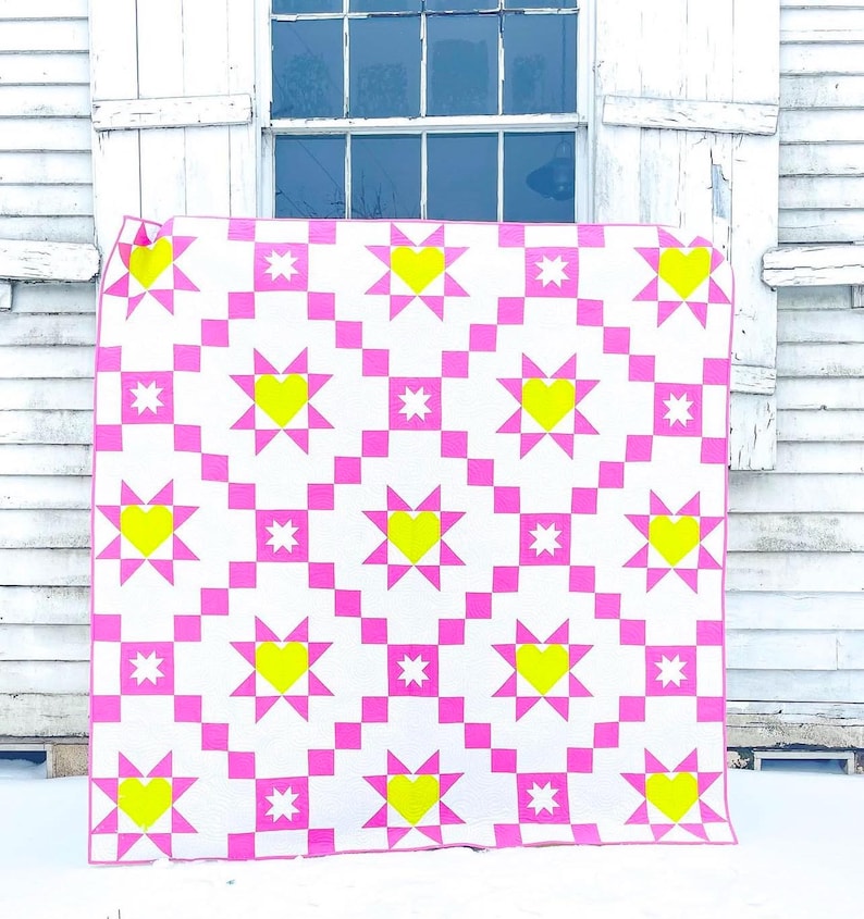 Puede incluir: Un edred&oacute;n hecho a mano con un patr&oacute;n repetitivo de cuadrados y estrellas de color rosa brillante, con corazones amarillos en el centro de las estrellas. El edred&oacute;n se muestra sobre un fondo blanco.