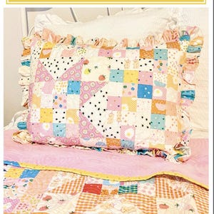 Puede incluir: Una funda de almohada rectangular con un diseño de patchwork de varios cuadrados en tonos pastel, incluyendo patrones de fresas, estrellas y huevos fritos. La funda tiene un borde con volantes y lleva el texto Sunny Days Pillow Sham de Amy Pinkos.