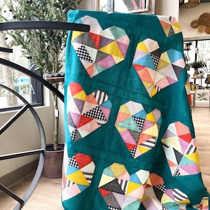 Peut inclure: Une courtepointe turquoise avec un motif de patchwork de cœurs géométriques colorés. La courtepointe est faite de différents tissus, dont du vichy noir et blanc, des rayures et des unis.