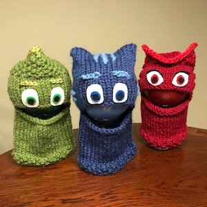 May include: Three knitted character hats with felt eyes. The hats are green, blue, and red. The green hat has a pointed top, the blue hat has cat ears, and the red hat has a wide brim.