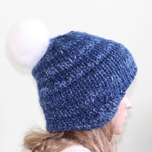 May include: A blue knitted beanie with a white pom pom. The beanie is made from a soft, textured yarn.