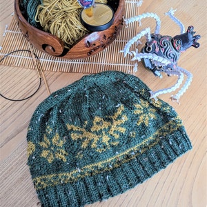 May include: A green and yellow knitted hat with a geometric pattern. The hat is made with a chunky yarn and has a slouchy fit.