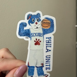 May include: A die-cut sticker featuring a blue anthropomorphic dog mascot wearing a white basketball uniform with the text SIXERS and a red paw print. The mascot holds a brown Spalding basketball and the text PHILA UNITE is printed vertically.