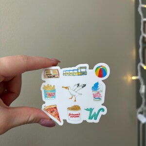 May include: A white sticker featuring a collection of colorful illustrations including a box of fries labeled Curley's Fries, a seagull, a cup of Johnson's Popcorn, a slice of pizza, a beach ball, a soft serve ice cream cup, and a green letter W.