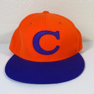 May include: An orange and blue baseball cap. The cap has a bright orange crown and a curved blue brim. A large blue letter "C" is on the front. This classic style hat is suitable for sports or casual wear. The cap is a classic style.