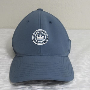 以下が含まれることがあります： ネイビーブルーの野球帽。つばがカーブしています。王冠が地球儀の中に入った白いグラフィックが特徴です。滑らかな素材でできており、上部にボタンが付いています。