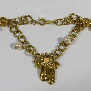 May include: Gold-toned charm bracelet featuring a chain link design. The bracelet includes charms of ballet slippers, pearls, and angel figures. The bracelet is approximately 7 inches in length.