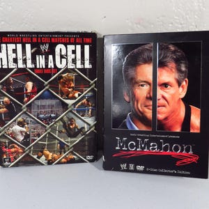 May include: Two WWE DVD sets. One is titled "Hell in a Cell" with images of wrestling matches behind a chain-link fence. The other is titled "McMahon" with a portrait of a man.
