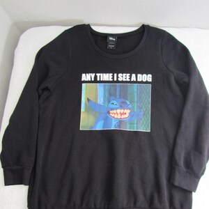 Peut inclure: Sweat-shirt noir &agrave; manches longues avec un dessin du personnage Disney Stitch et le texte "ANY TIME I SEE A DOG". L'image montre Stitch avec un grand sourire. Le sweat-shirt a un col rond et des poignets c&ocirc;tel&eacute;s.
