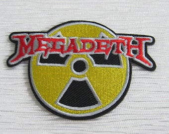 May include: A circular embroidered patch featuring a yellow and black radiation symbol. The word MEGADETH is stitched in red with a black and white outline across the top of the symbol. The patch has a black border and textured stitching.