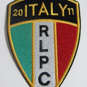以下が含まれることがあります： 黒と金の刺繍が施されたパッチで、"20 ITALY '11"という文字と、緑、白、赤の背景に白い文字で"RLPC"という文字が書かれています。