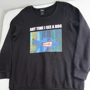 Peut inclure: Sweat-shirt noir &agrave; manches longues avec un dessin du personnage Disney Stitch et le texte "ANY TIME I SEE A DOG". L'image montre Stitch souriant. Le sweat-shirt a un col rond.
